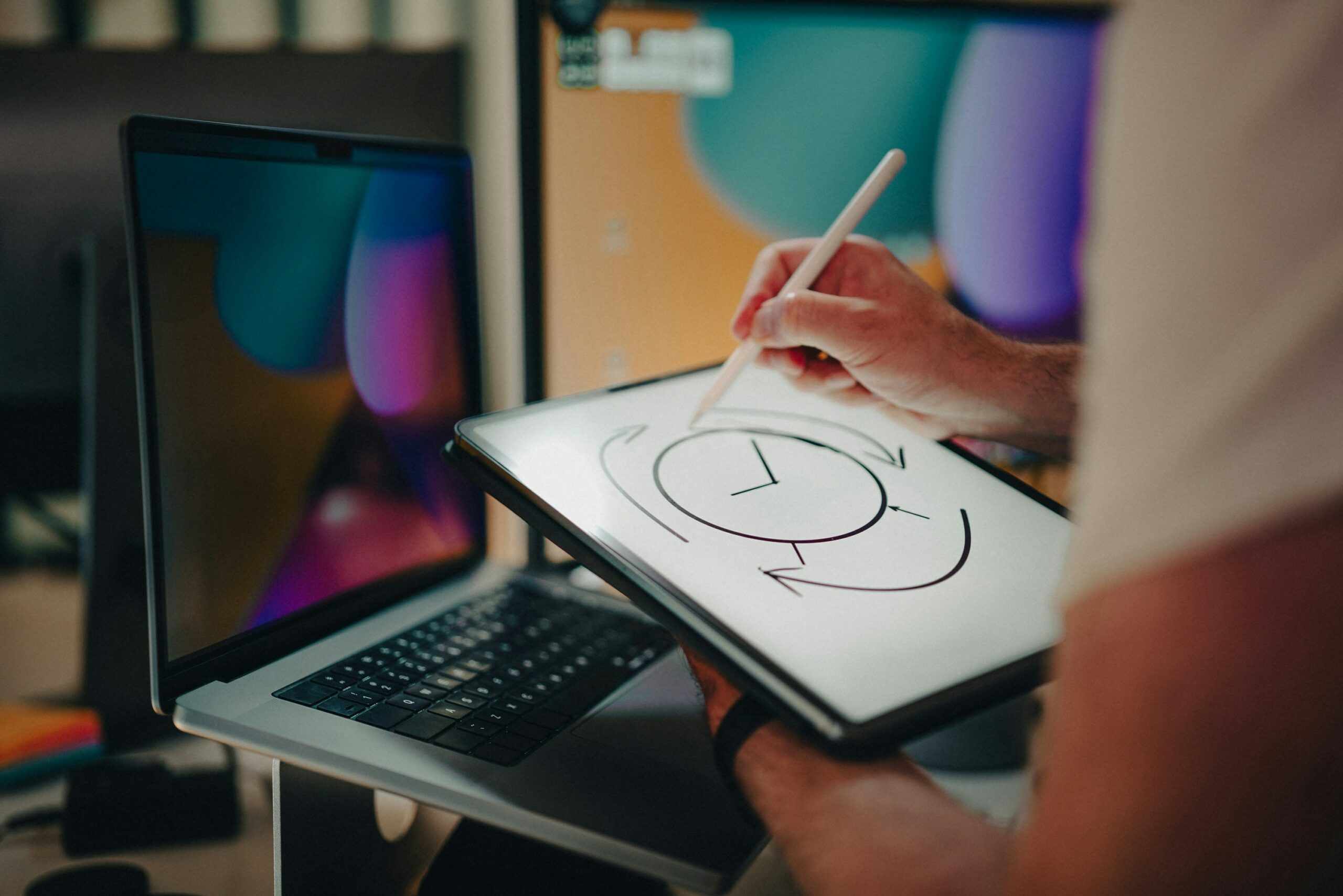 person in front of a laptop drawing a clock on a tablet