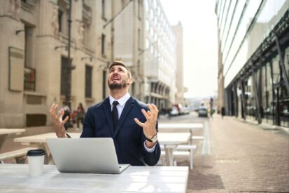 software testing on a laptop at the middle of the street, a white man look at the sky with his hand up, in apparent suffering